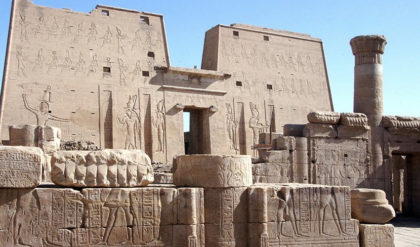 The Temple of Horus in Edfu with its massive stone pylons, detailed relief carvings, and well-preserved ancient Egyptian architecture under a clear sky.