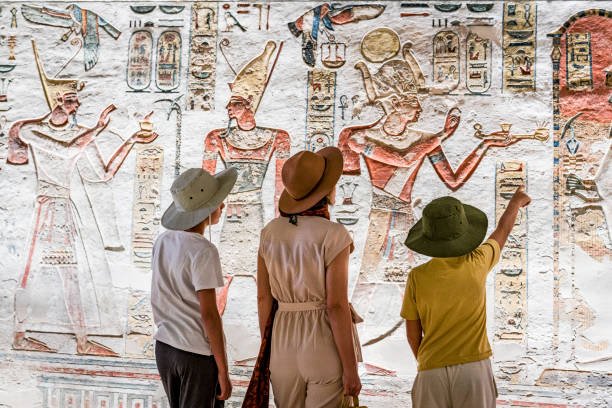 Mother and sons looking at the colorful pharaohs reliefs and paintings inside Ramses IX Tomb, Valley of the Kings, Egypt